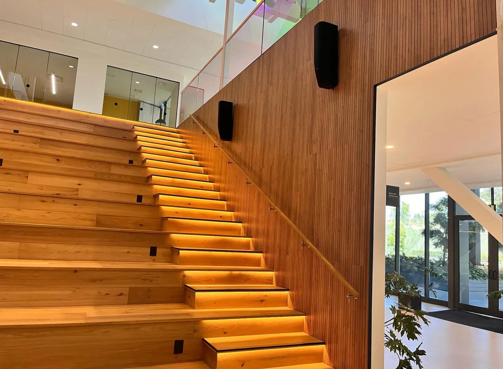 Escalera y grada de madera junto a pared revestida con lamas acústicas en la Universidad de la Libertad, México