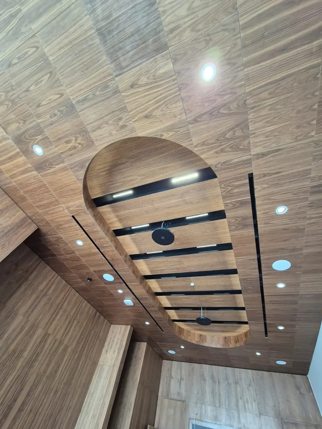Techo acústico de madera microperforada con isla ovalada de lamas e iluminación lineal en el Alhi Bank de Jordania